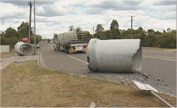 A large concrete pipe slipped of a truck and broken on the road and nature strip on the roadside.