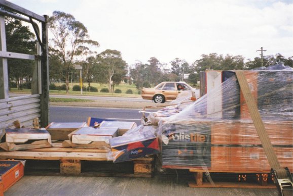 Side view of a trailer carrying bulk load boxes on a pallet restrained using plastic wrapping and one strap only.