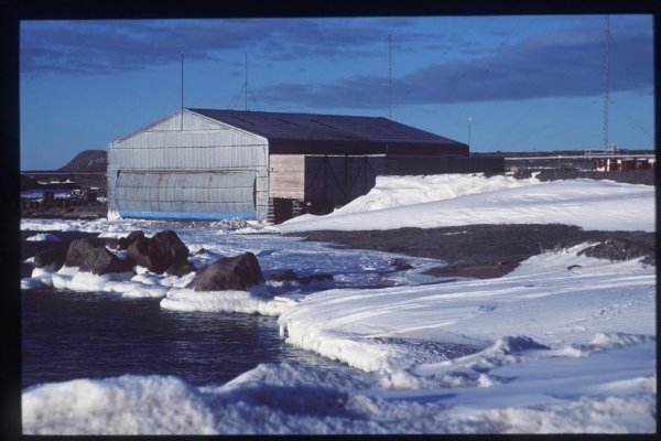 Exterior photograph of corrugated and galvanised steel hangar with snow in foreground in 1997