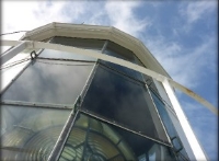 Photograph showing close up of glass glazing panes. Handrail for external catwalk visible in front of panes, and lighthouse lens visible behind panes inside lantern house.  