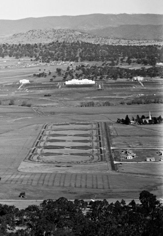 An oblique photograph with hills in the background, buildings in the centre ground and trees in the foreground.