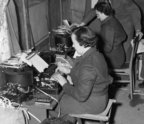 Two people in uniform typing at a machine.


