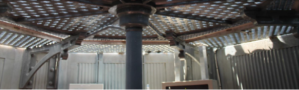 Photograph showing underside of cast iron lattice floor, including a cast iron brackets supporting the floor. Bracket is attached to a corrugated internal wall. A cast iron post supports the centre of the lattice floor above.  