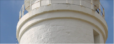 Photograph showing external, white, round stone base of a lighthouse balcony. Handrails can be seen protruding from balcony floor above.