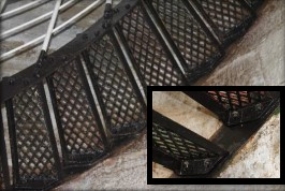 Photograph showing black, cast iron staircase with white wrought iron railing, wrapped around stone wall.