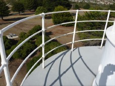 Photograph showing white iron pipe railing curved around edge of grey balcony. 