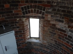 Photograph of curved, internal brick wall of lighthouse. Rectangular window is set into brick wall.