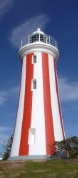Photograph showing white lighthouse tower with red vertical stripes against blue sky. 
