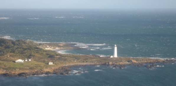 Photograph of a white lighthouse tower beside a coastline.