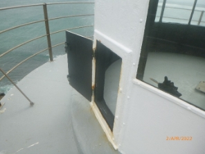 Photograph of small door hatch fitted to white lantern house. Door is opened out onto the balcony.