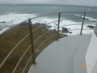 Photograph of a grey balcony floor wrapped around a lantern house. Stainless steel balustrades and stanchions are bolted to the outer edge. 