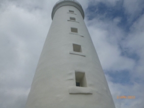 Photograph showing white lighthouse tower with five window openings cut into tower.