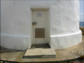 Photograph showing a door fitted into the base of a white lighthouse tower. 