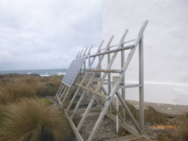 Photograph showing solar panel racks surrounded by grassy vegetation.