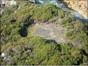 Photograph of square concrete slab amongst low-lying scrub 