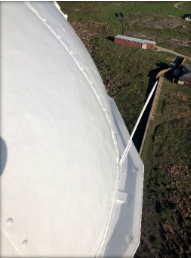 Photograph of dome roof and gutter. Windbreak wall and service building can be seen on ground below.