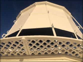 Photograph of white lantern house covered in white blanking panels, with white lattice catwalk fitted to external base.