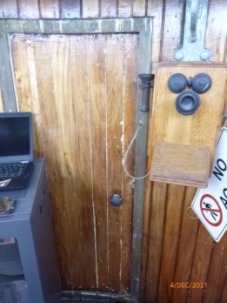 Photograph of timber-lined door fitted in curved lantern room. An old telephone with attached receiver is mounted on wall beside door.