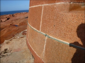Photograph of granite blocks and mortar used in lighthouse tower. Rocky landscape seen beside tower.