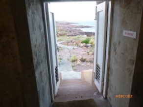 Photograph of open double doors leading out of lighthouse tower. Winding pathway and rocky landscape seen outside.
