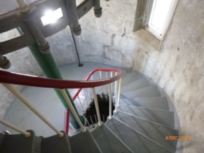 Photograph of winding staircase wrapping around curved internal wall to floor below. A central column travels through centre of winding stairs to floor above.