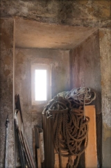 Photograph of small window set into thick granite walls. Pallets and bundles of rope sit in front of the window.