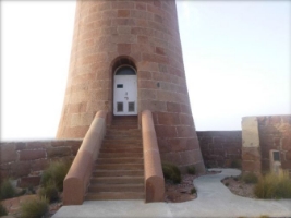 Photograph of base of granite lighthouse tower, with staircase leading up to set of white double doors.