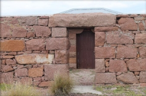 Photograph of granite windbreak wall with small access opening leading to small granite store shed.