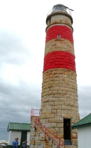 Photograph showing tall stone lighthouse tower with two red bands painted around external walls.