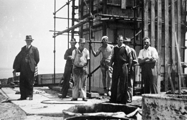 Black and white photograph showing a group of workers standing beside lighthouse tower under construction.