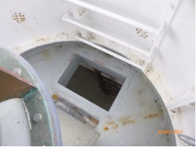 Photograph showing small rectangular floor hatch cut into circular lantern room floor with white lantern rungs attached to wall panels.