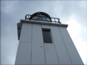 Photograph showing one side of a white lighthouse tower with rectangular window cut into concrete wall. 