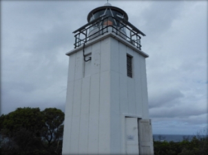 Photograph showing concrete lighthouse tower with lantern house sitting on small square balcony. 