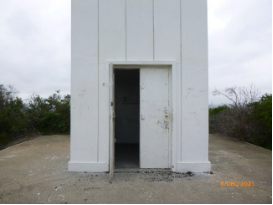Photograph showing lighthouse tower doors standing ajar at base of lighthouse tower.