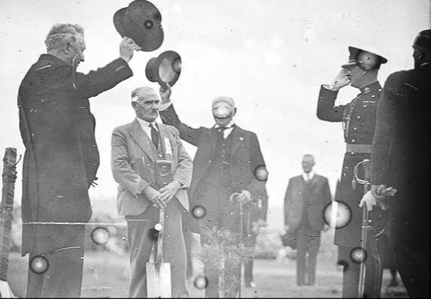 The Duke of Gloucester with a shovel planting lone pine with 5 other people around.