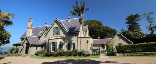 A picture of Kirribilli House depicting an entrance to the property with bushes by the windows. A side-gate to the right as an external entry point to the property, with hedges to its right.