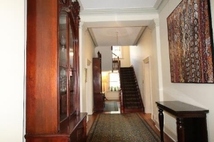 A picture of the Kirribilli house stair hallway with wooden cabinets, tables and art on the walls.