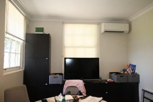 A picture of Kirribilli House Staff Room which shows a fridge, round table with two chairs, Television on top of drawers and an air-conditioner.