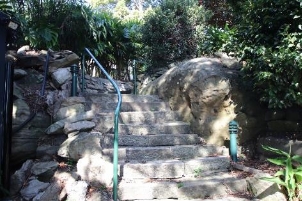 A picture of Kirribilli House garden stairs with green railing, green garden lights and surrounding rocks and bushes.