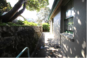 A picture of the side of Kirribilli House with a narrow concrete path and stone wall parallel to the property and path