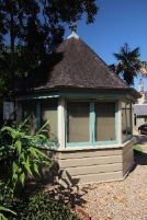 A picture of the guard house at Kirribilli House with blue framed windows, dark brown pointed roof and trees around the house. 