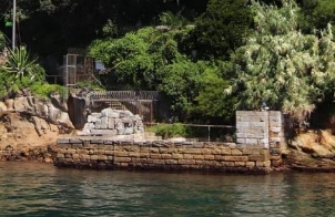 A picture of the Kirribilli House Boat Harbour showing the harbours dark blue water, water stained stone walls and large trees and bushes all around. 