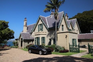 A picture of Kirribilli House with a black car parked in front and the green side gate opened.