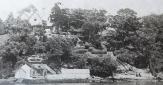 A black and white image from the harbour looking at Kirribilli House, surrounded by large trees and vegetation. 
