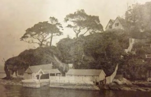 A sepia tone picture of the Kirribilli House bathing pool and boat harbour close by to the harbour and surrounded by large trees and a body of water. 
