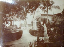 A sepia tone image of the previous Kirribilli House entry way showing more vegetation surrounding the property and a small statue amongst the entry way garden. 