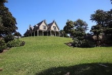 A picture of Kirribilli House from the bottom of the large green grass slope it is perched up on. 