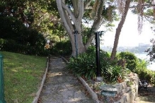 A picture of a stone path and wall surrounded by grass, trees and bushes at Kirribilli House