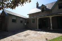 A picture of the south terrace of Kirribilli House, showing the stone pavement before the grass lawns and windows, columns and entry ways on this side of the house