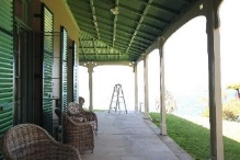 A picture of a veranda with outdoor chairs by the green framed windows, adjacent to the columns before the property's lawns